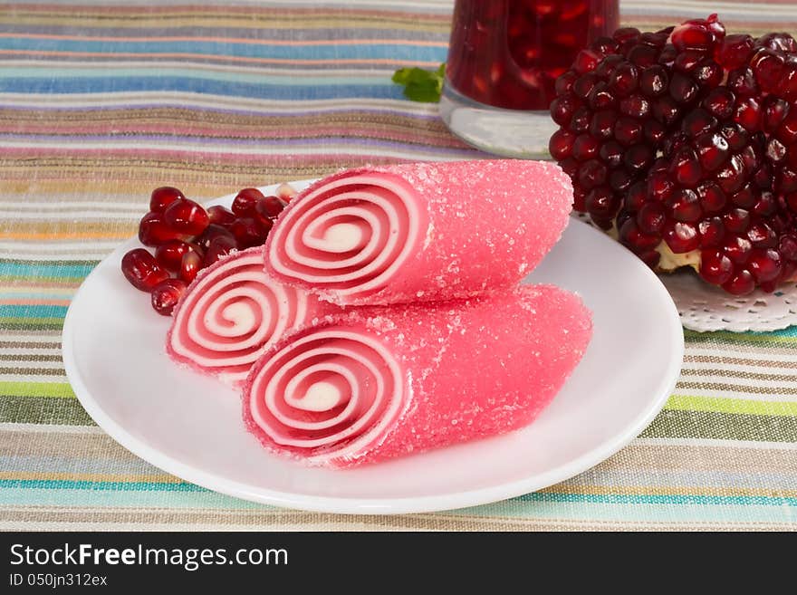 Red candy fruit on a plate with pomegranate, closeup