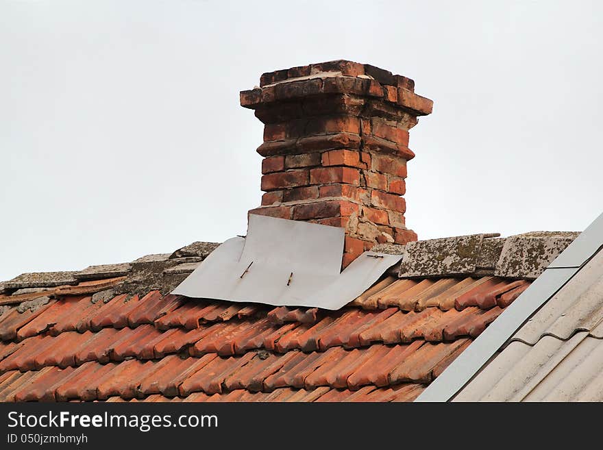 Old pipe from the furnace on the roof out shingles, on grey sky