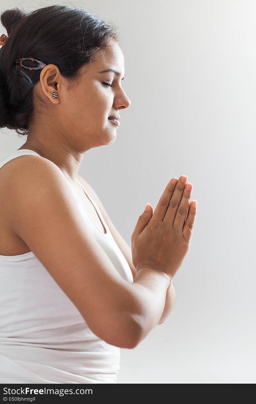 A beautiful Young Indian girl in white top doing meditation by joining hands. A beautiful Young Indian girl in white top doing meditation by joining hands