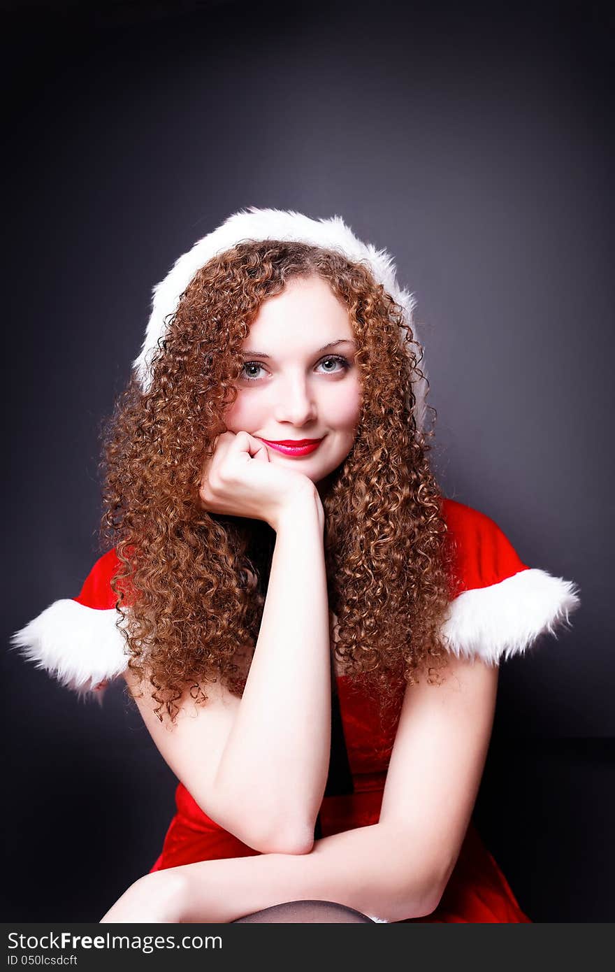 Portrait of pretty curly girl in Santa costume dark background