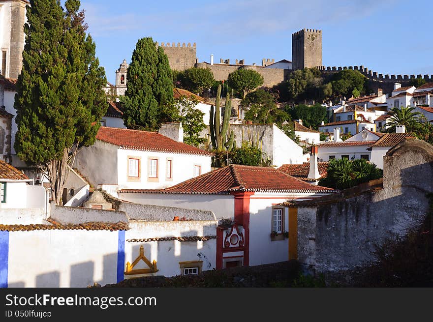 Old beautiful houses in medieval city of Obidos, Portugal with castle wall in background