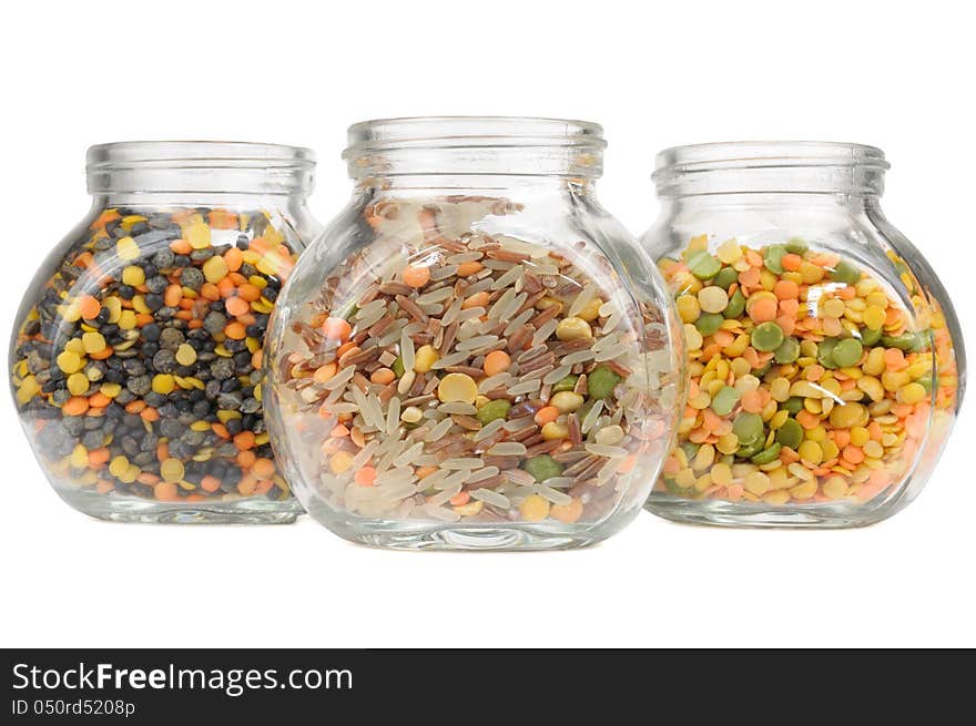 Three glass jars with assorted cereals (lentils, red and parboiled rice, split peas) isolated on a white background - horizontal orientation. Three glass jars with assorted cereals (lentils, red and parboiled rice, split peas) isolated on a white background - horizontal orientation