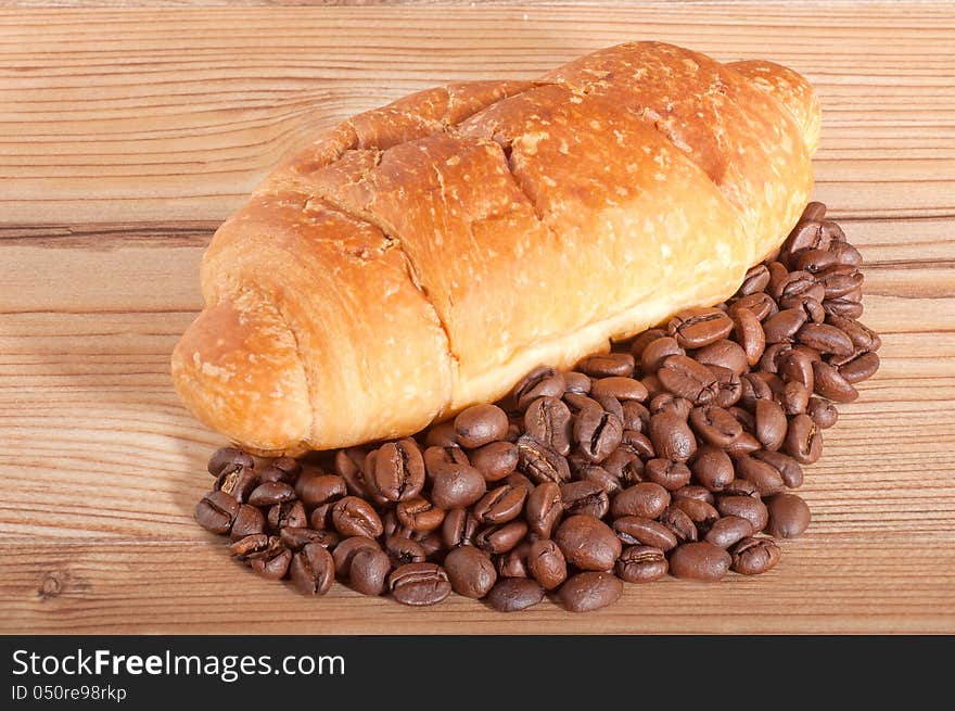 Croissant with coffee beans on wooden background.