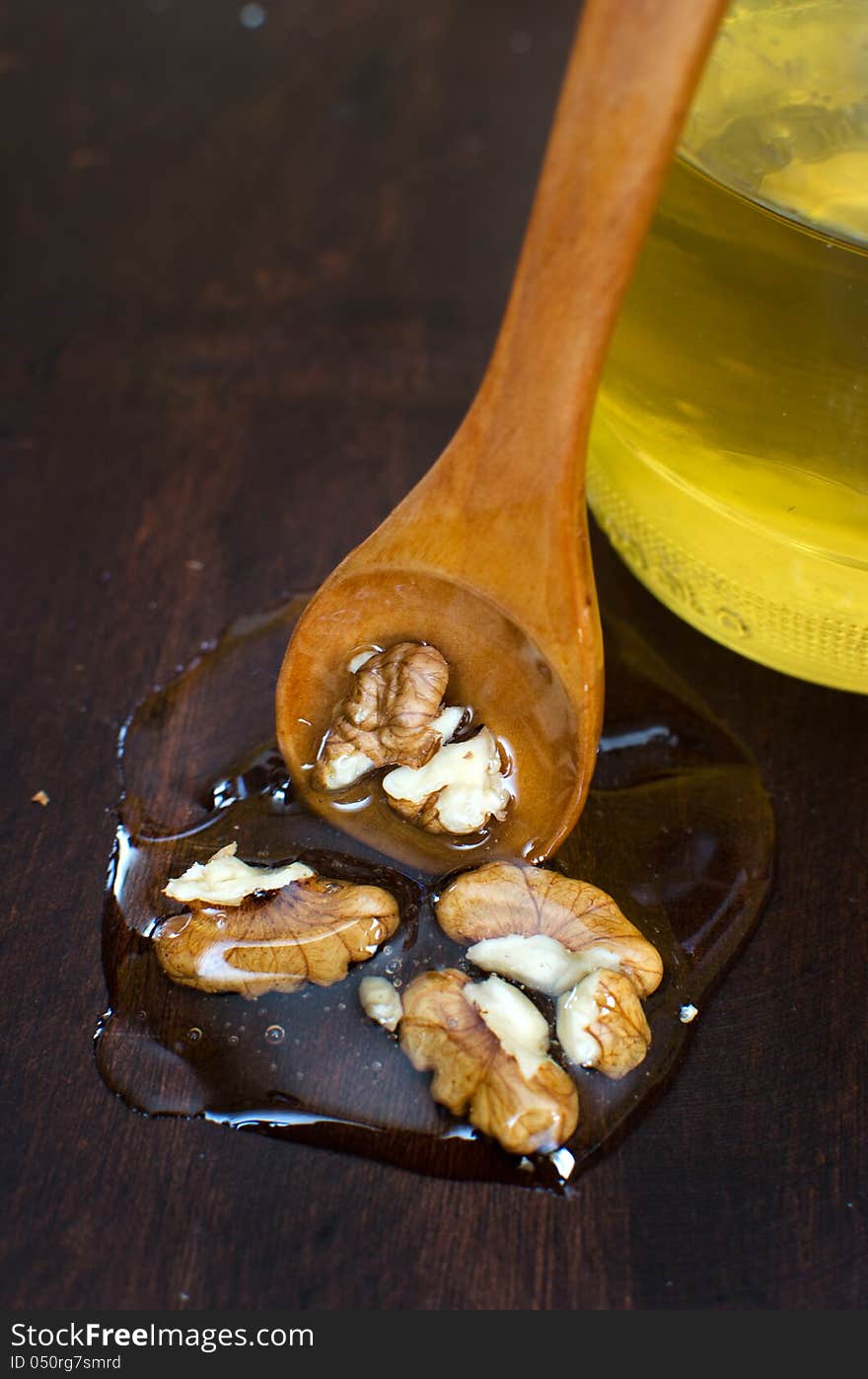 Wallnuts in honey on wooden background with wooden spoon and honey jar