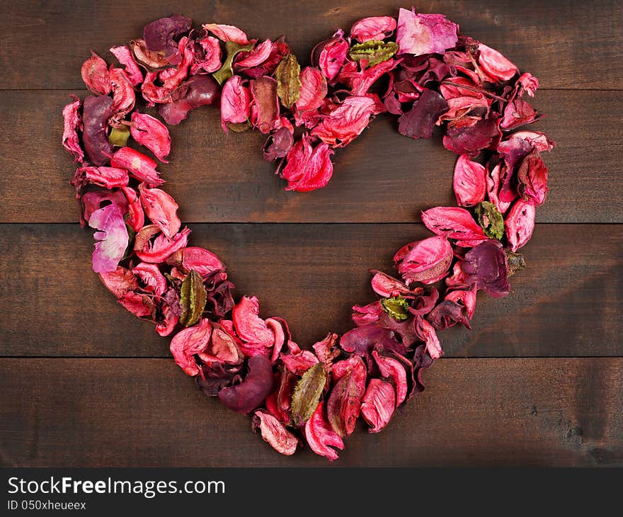 Flower Petals forming a heart shape against wooden background