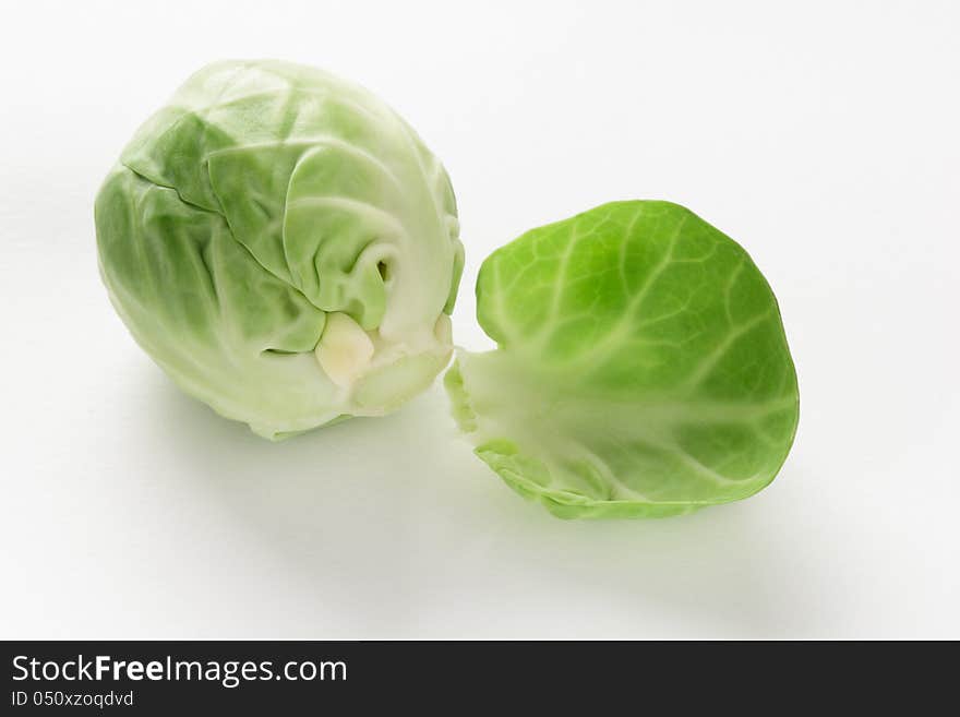 Head or bud of a fresh green brussel sprout, brassica oleracea, with a single loose leaf on a white studio background. Head or bud of a fresh green brussel sprout, brassica oleracea, with a single loose leaf on a white studio background