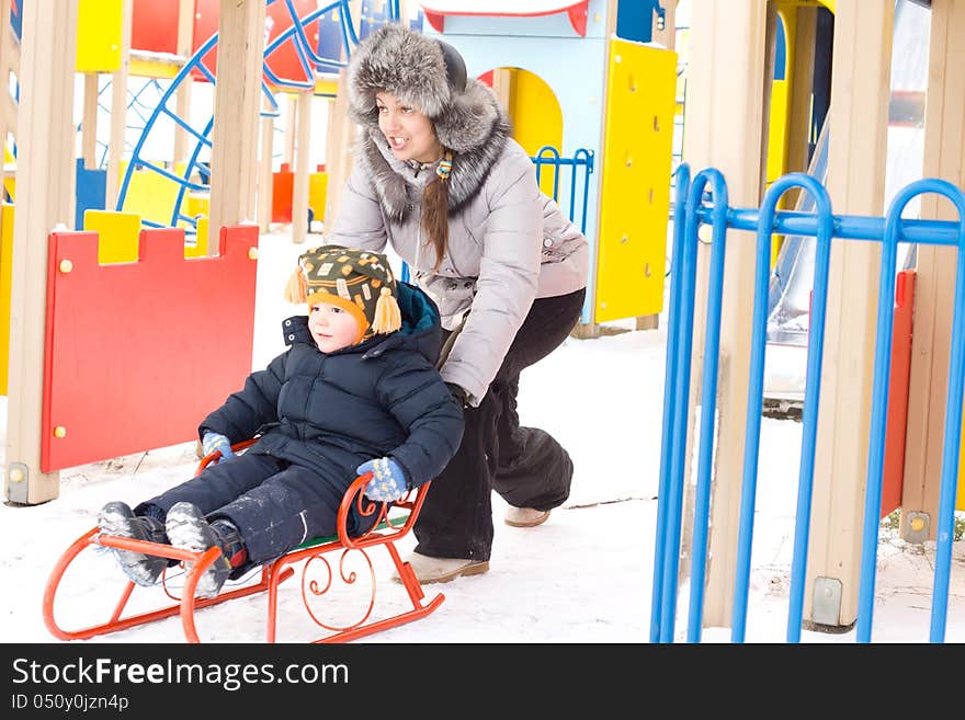 Mother pushing her son on a winter sled