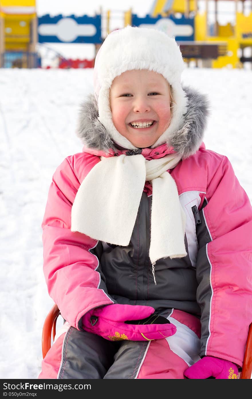 Beautiful smiling little girl sitting on a sled in snow laughing at the camera as she enjoys the freedom of a winter playground. Beautiful smiling little girl sitting on a sled in snow laughing at the camera as she enjoys the freedom of a winter playground