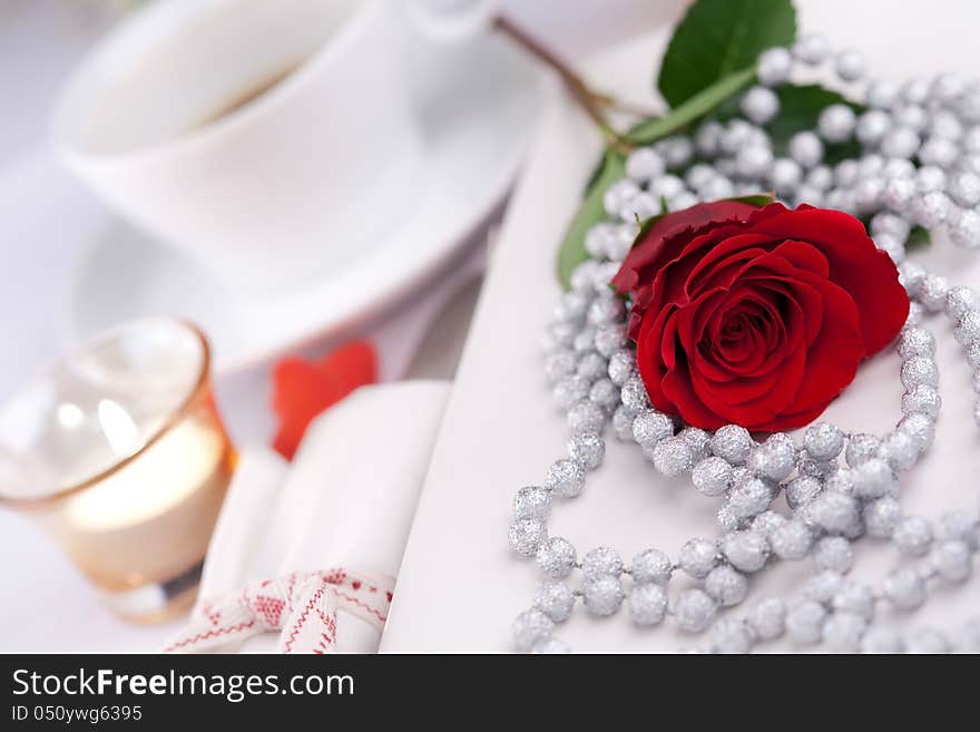 Romantic table setting with a single red rose, decorative necklace and candle to celebrate Valentines day, anniversary, wedding or engagement