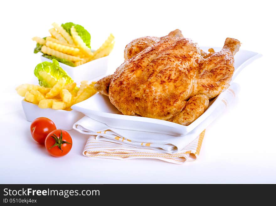 Crisp golden roast chicken served with side dishes of fresh fried crinkly French fries and ripe red tomatoes for a delicious meal