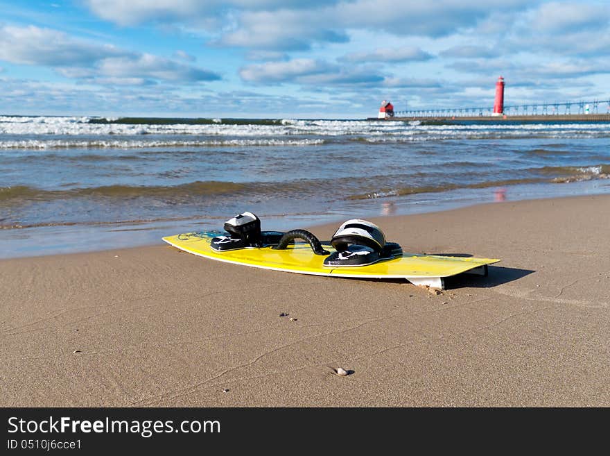 A yellow kiteboard on a Lake Michigan beach with red lighthouse in the background. A yellow kiteboard on a Lake Michigan beach with red lighthouse in the background