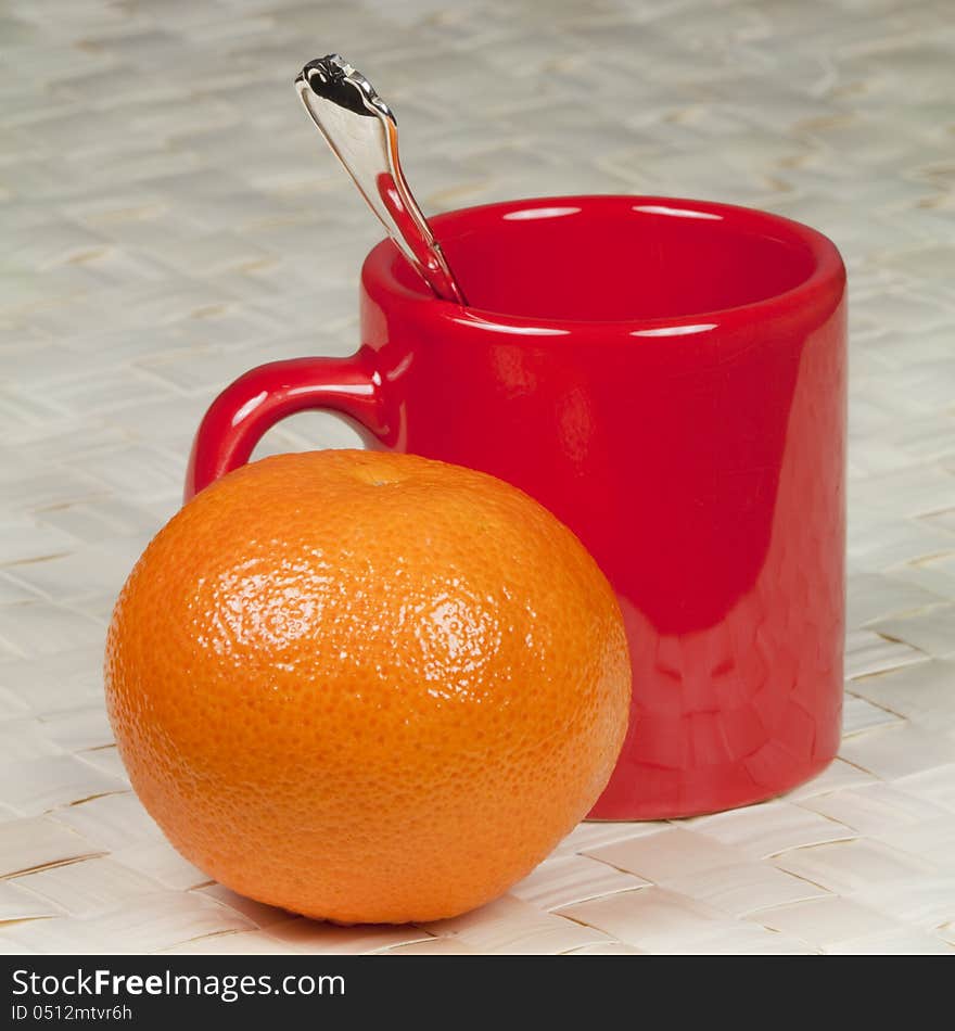 A cup for coffee, a silver spoon and mandarin on a mat made of palm leaves. A cup for coffee, a silver spoon and mandarin on a mat made of palm leaves