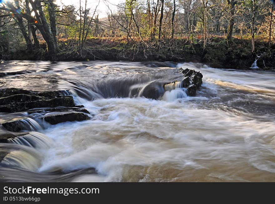 Swollen river with swirling water cascading over rocks. Swollen river with swirling water cascading over rocks