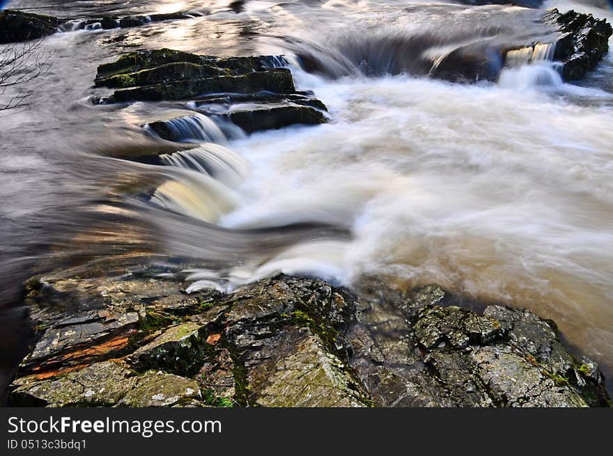 Swollen river with swirling water cascading over rocks. Swollen river with swirling water cascading over rocks