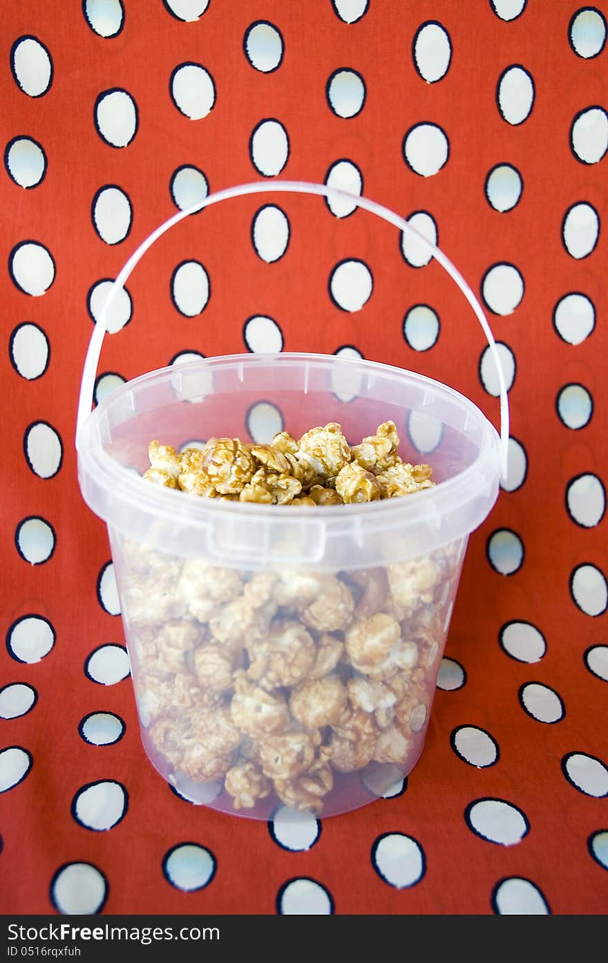 Caramel popcorn in plastic bucket on red background