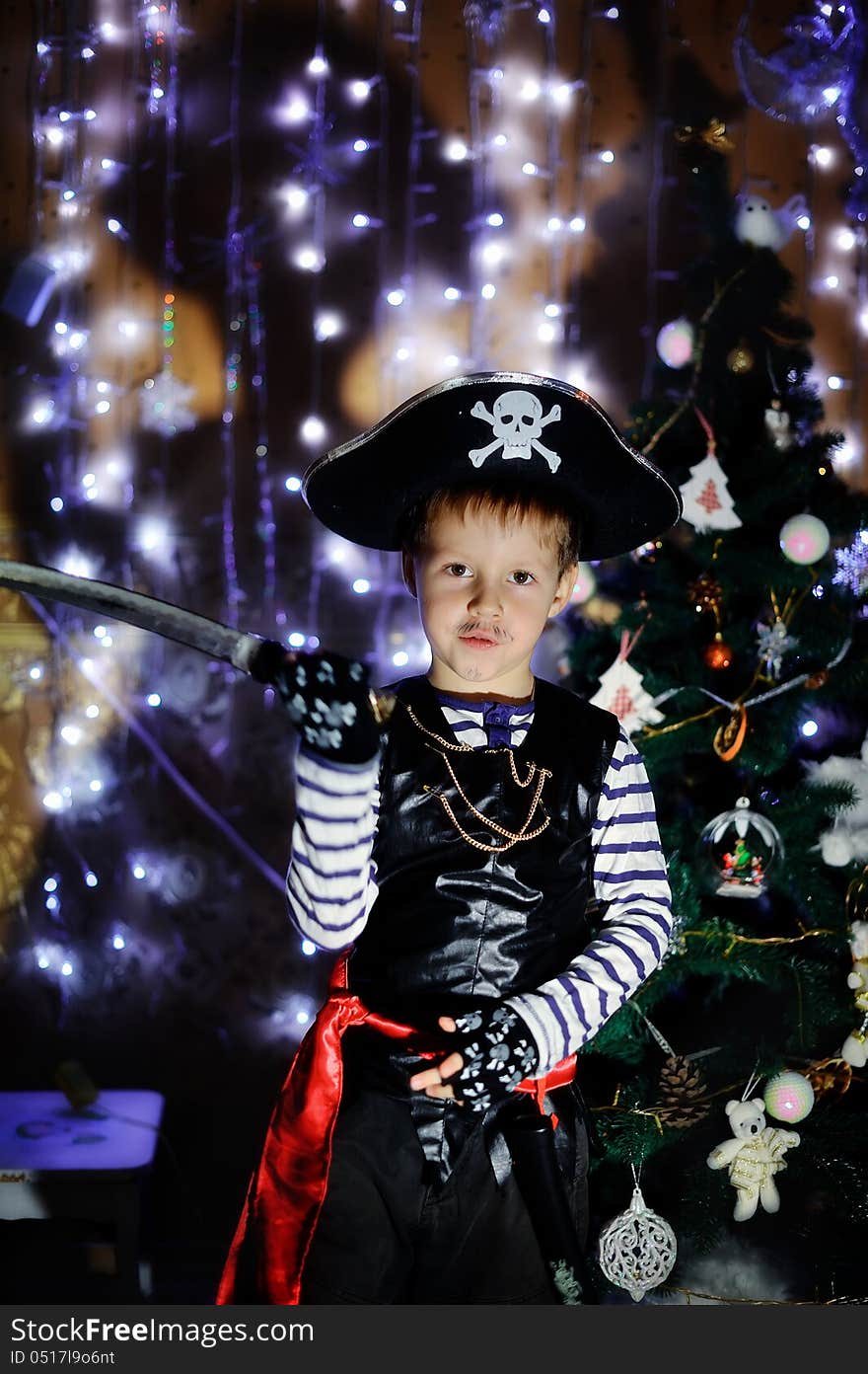 The boy in clothes of the pirate against a New Year tree poses. The boy in clothes of the pirate against a New Year tree poses