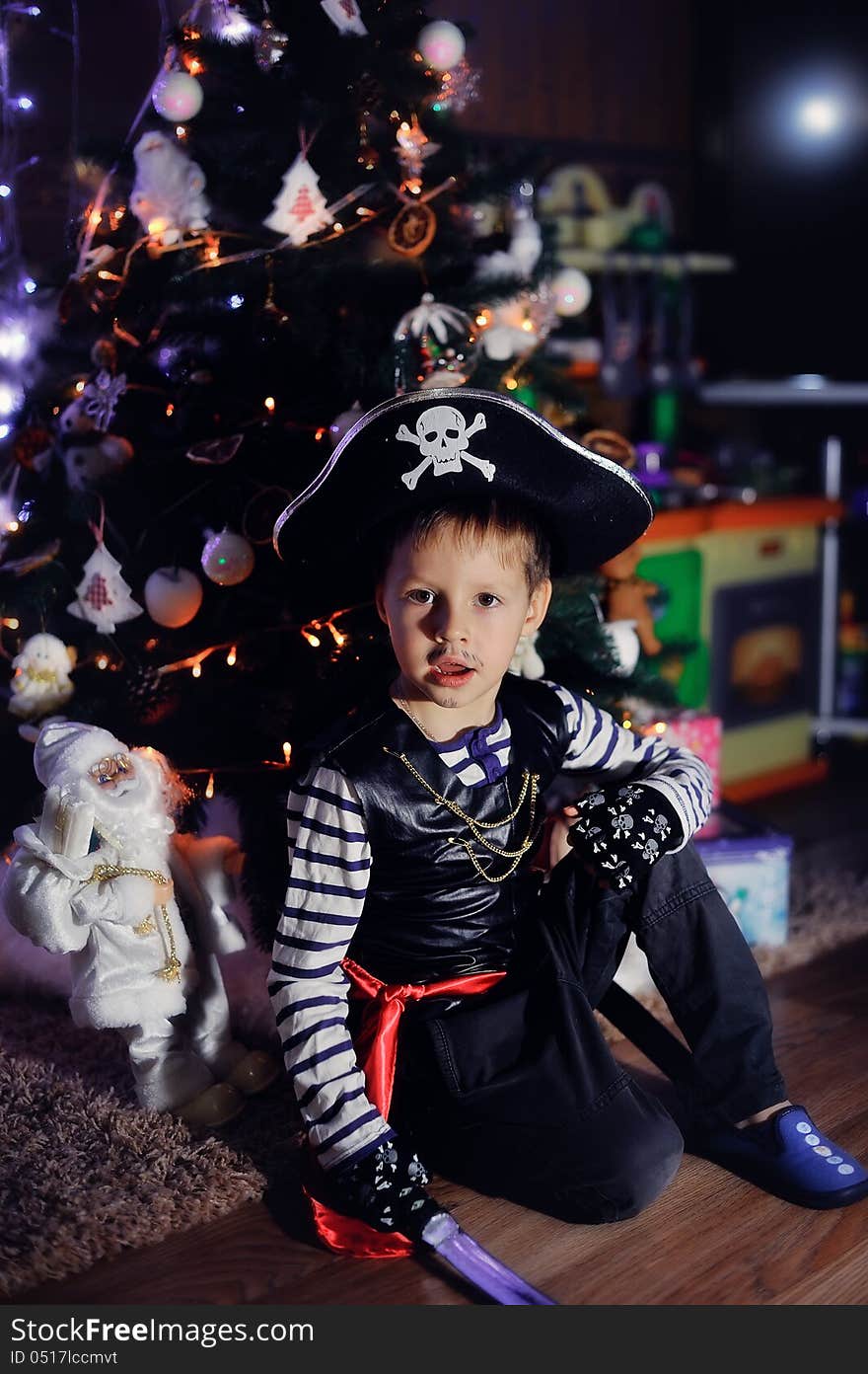 The boy in clothes of the pirate against a New Year tree poses. The boy in clothes of the pirate against a New Year tree poses