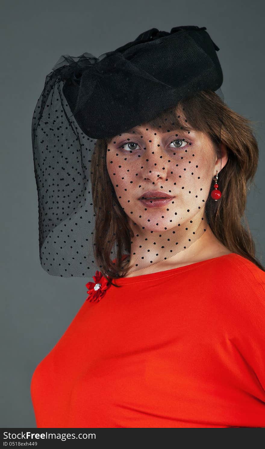 Portrait of young girl in black hat with veil and red dress