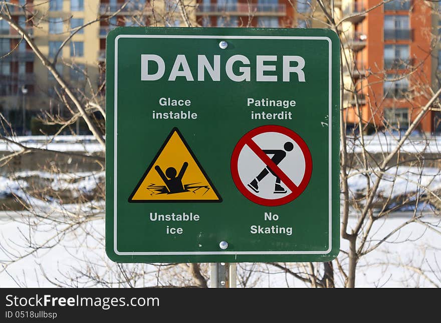 Bilingual sign to advise of the danger of thin ice with river in the background. Bilingual sign to advise of the danger of thin ice with river in the background