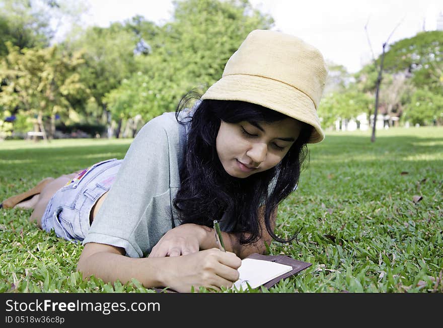 Beautiful teenage girl writting book, against green of summer park.