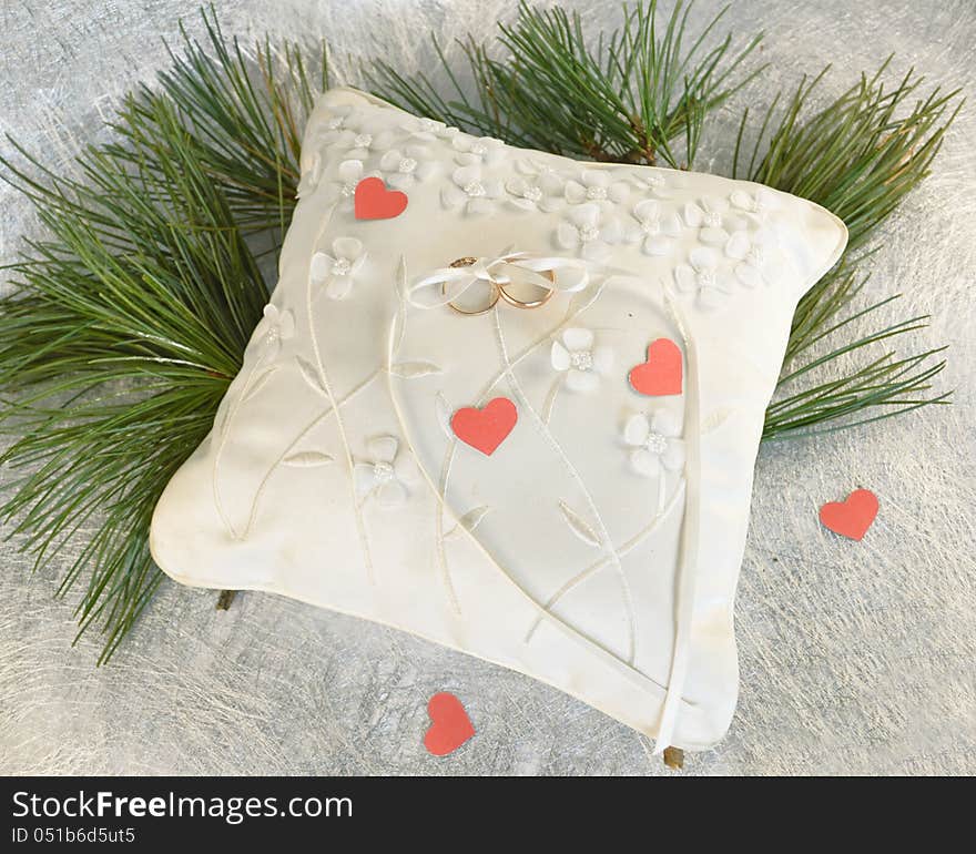 Wedding pillow with the golden rings, pine needles and hearts cut out of paper