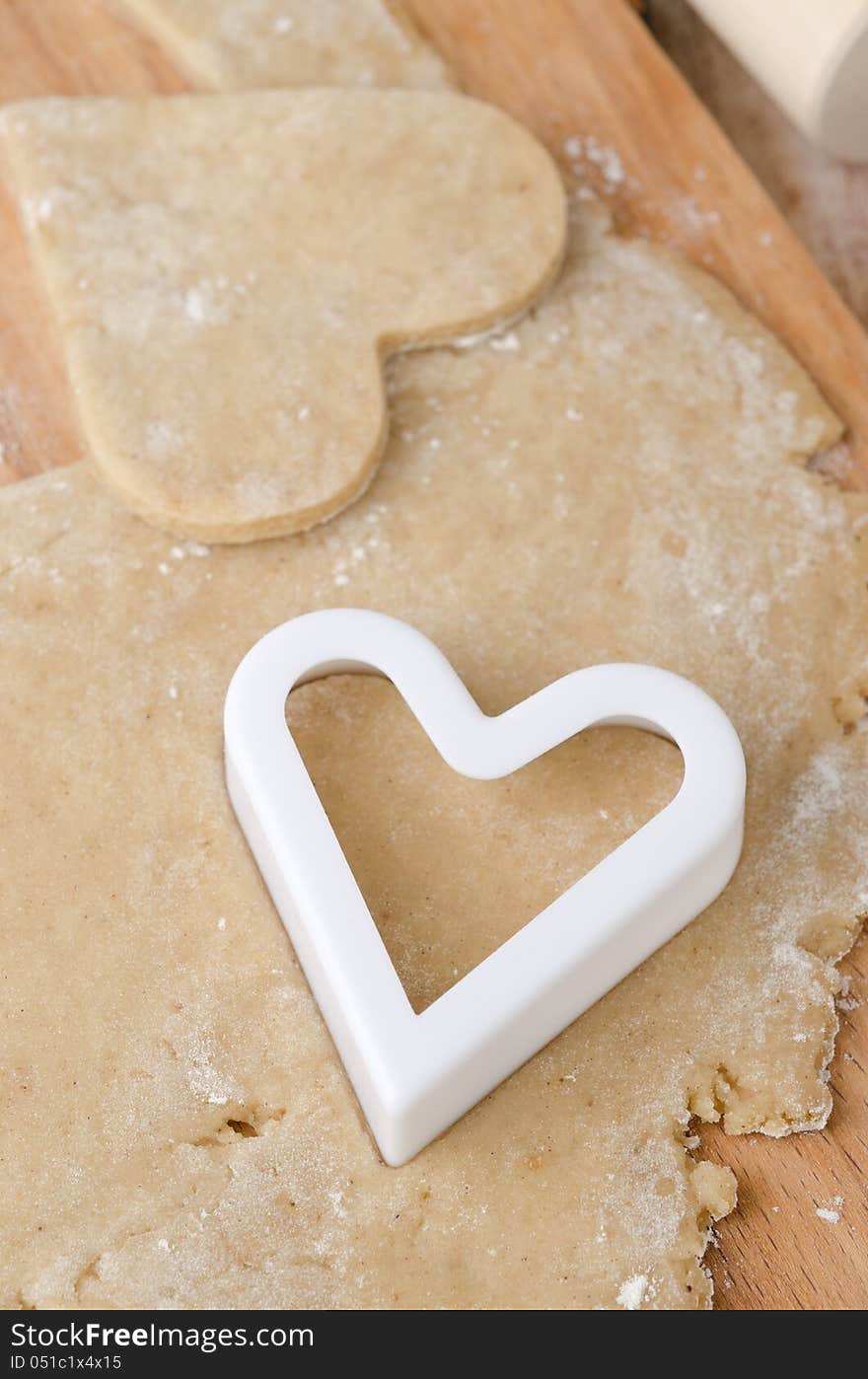 Cookie cutters in the form of heart in cookie dough on a wooden cutting board