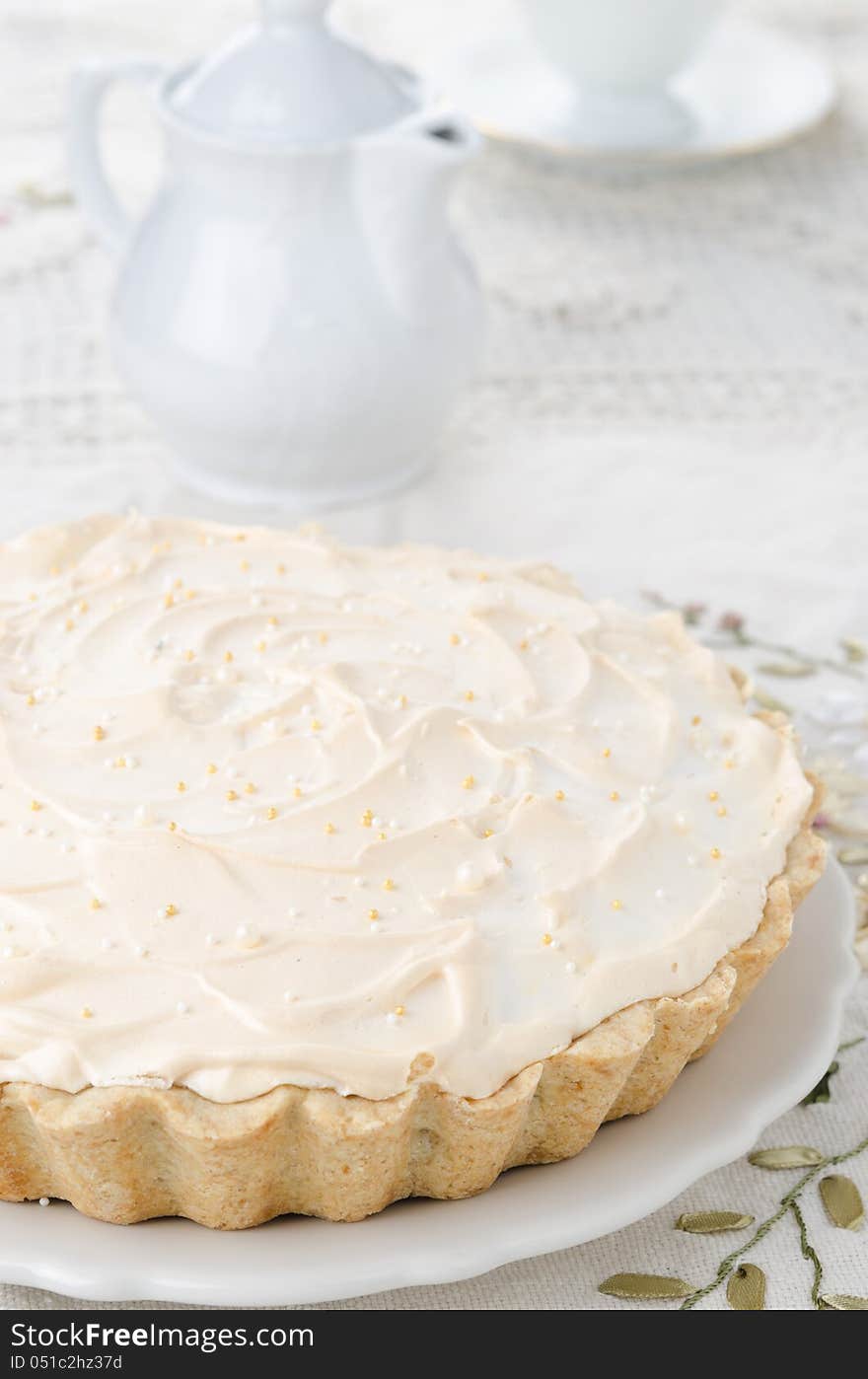 Lemon tart with meringue on a white plate. Teapot and cup in the background. Lemon tart with meringue on a white plate. Teapot and cup in the background.