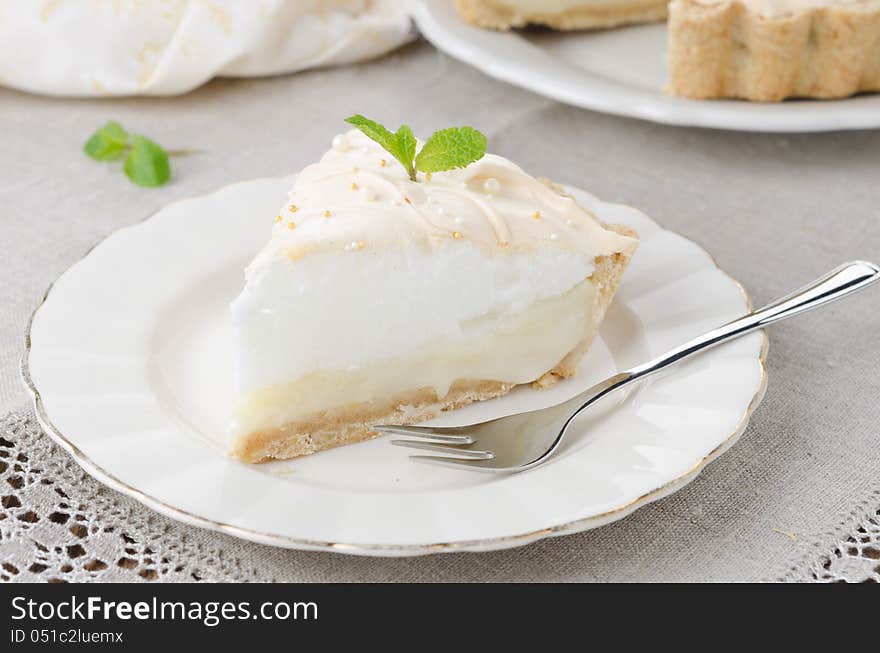 Piece of lemon tart with meringue decorated with fresh mint on a plate closeup