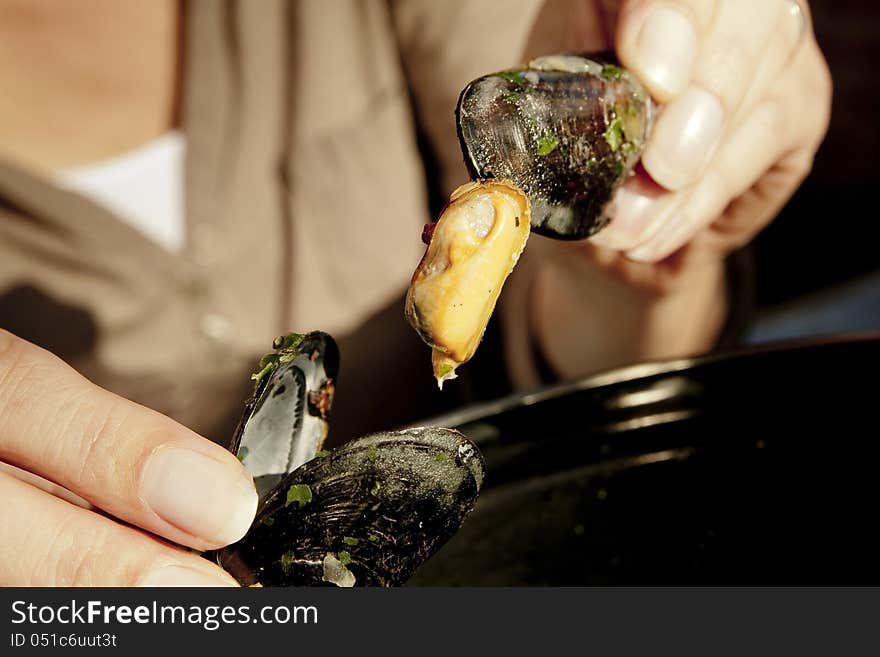 Woman taking a mussel out of a shell. The scene is situated in a warm late afternoon sunlight. She is eating out of a pan which is partially visible. Woman taking a mussel out of a shell. The scene is situated in a warm late afternoon sunlight. She is eating out of a pan which is partially visible.