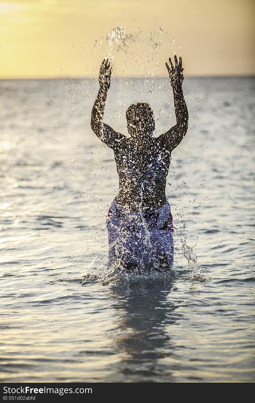 A Young Girl Splashing Water in the Ocean with her hands up in the air