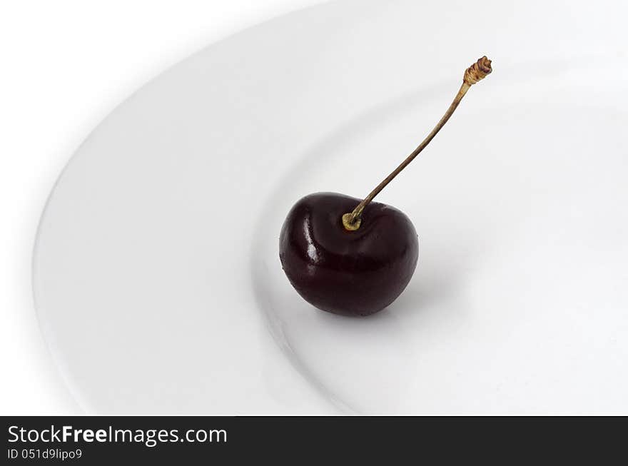 One cherry on a white plate on a white background.