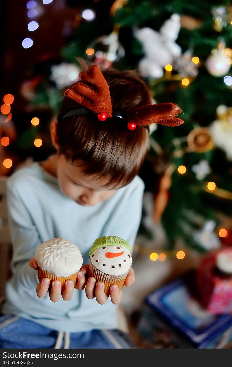 The boy with small horns of a deer under a New Year tree with beautiful fruitcakes in hand. The boy with small horns of a deer under a New Year tree with beautiful fruitcakes in hand