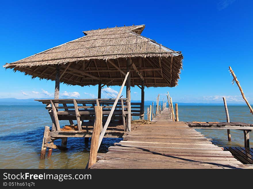 Old wooden boat dock, going far out to sea. Hut with a thatched roof. Blue sky and white clouds. Beautiful sea landscape.