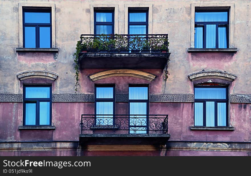 Facade of an old house with metal balconies and overgrown with flowers