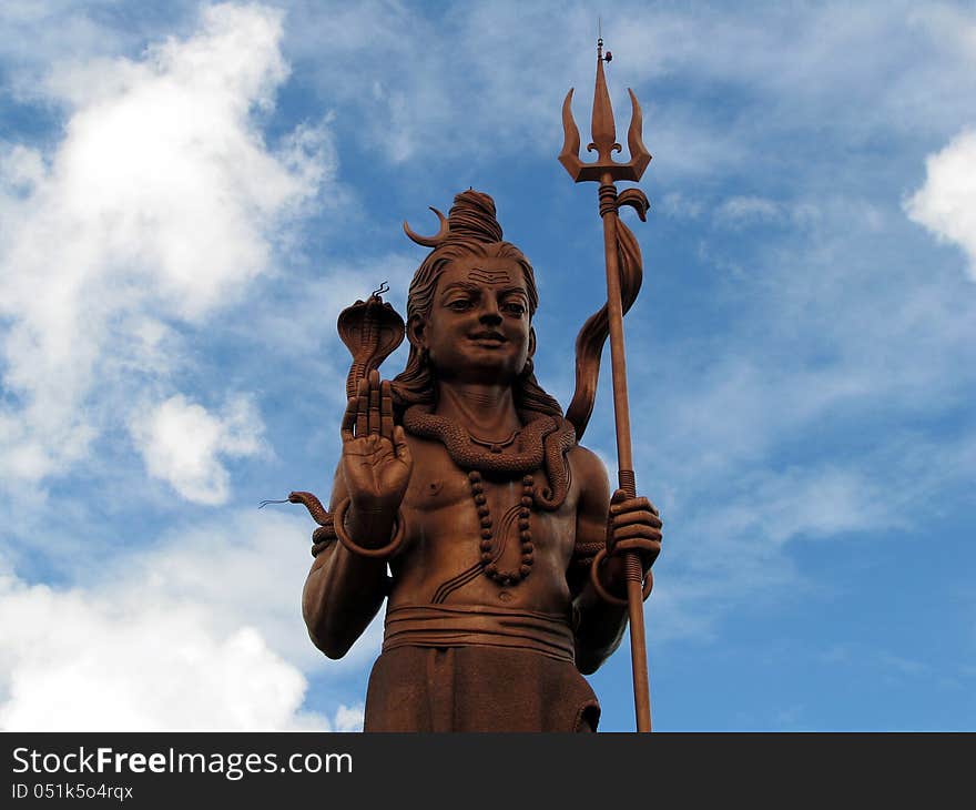 Shiva statue at GAnga Talao against the blues sky and clouds in Mauritius.