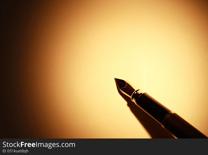 Closeup of stylish fountain pen on yellow paper surface with beam of light. Closeup of stylish fountain pen on yellow paper surface with beam of light