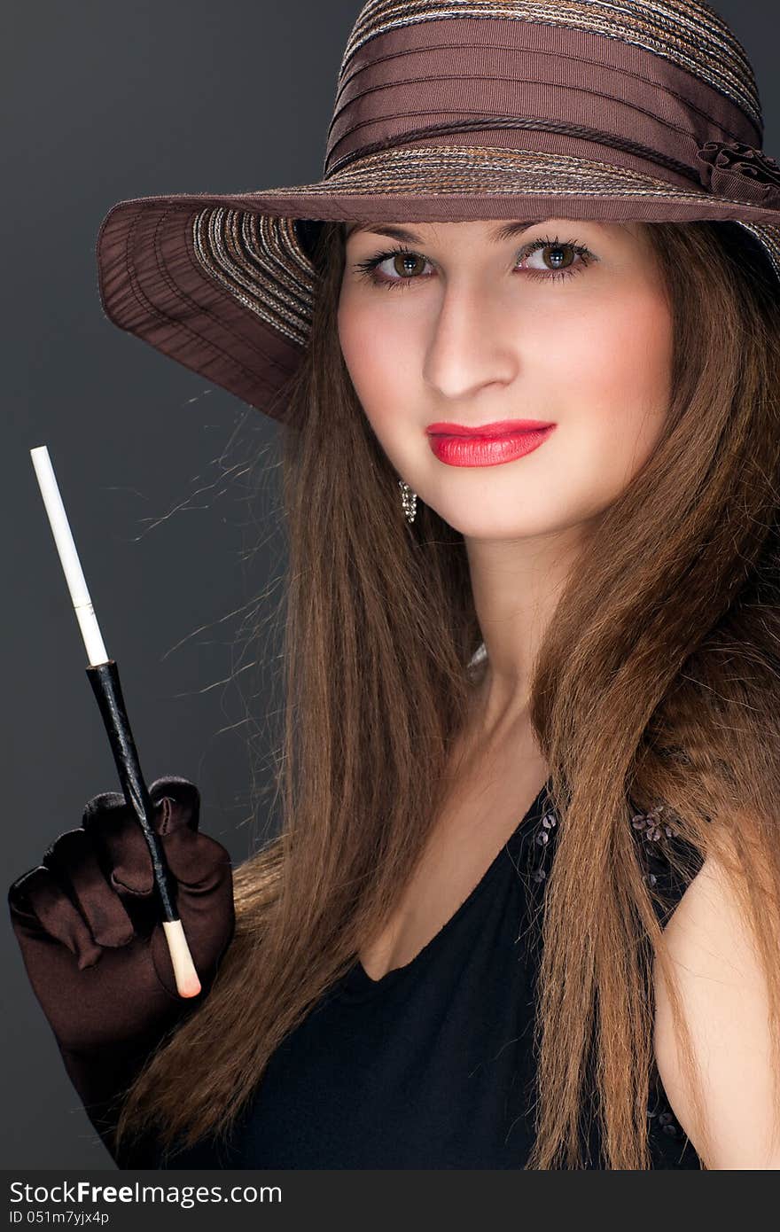 Portrait of a beautiful woman in black dress, brown hat and mouthpiece with cigarette. Portrait of a beautiful woman in black dress, brown hat and mouthpiece with cigarette