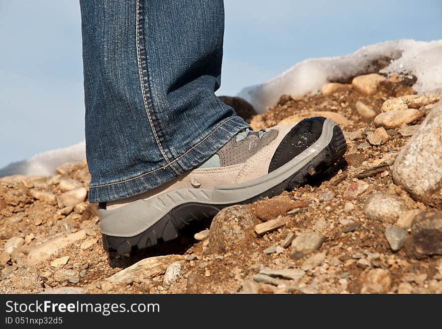 Foot of a woman trekker, climbing a rocky mountain, with snow in the background, against the pale blue sky. Foot of a woman trekker, climbing a rocky mountain, with snow in the background, against the pale blue sky