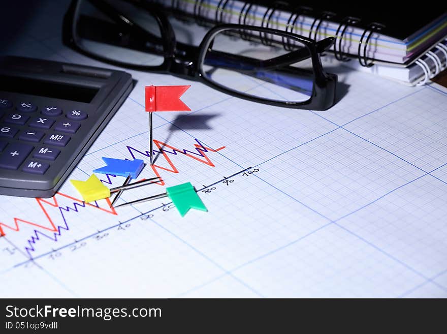 Calculator near red pin and spectacles on graph paper with diagram. Calculator near red pin and spectacles on graph paper with diagram