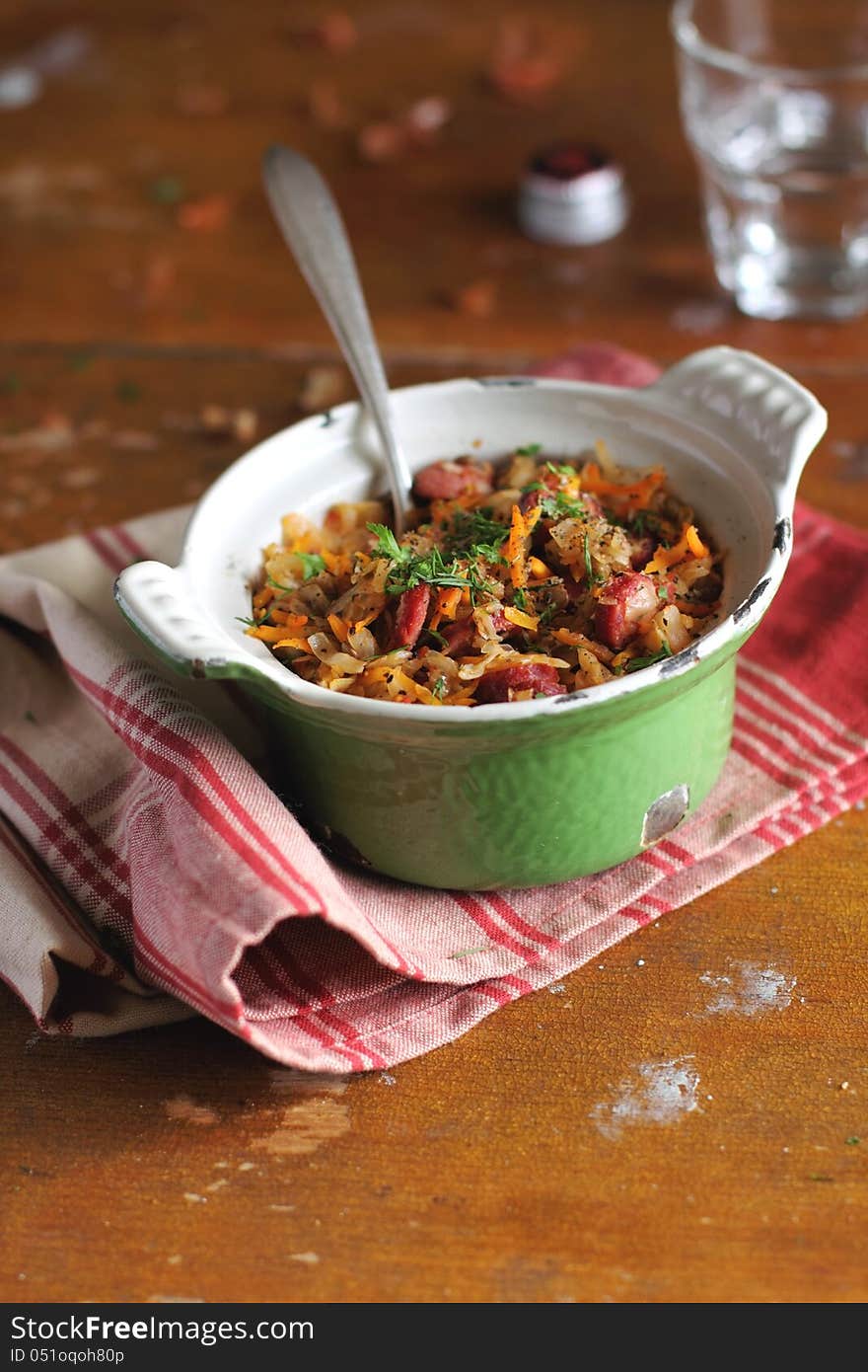 Stewed cabbage with sausages, carrots and lentil in a green sauce pan on a kitchen towel. Stewed cabbage with sausages, carrots and lentil in a green sauce pan on a kitchen towel