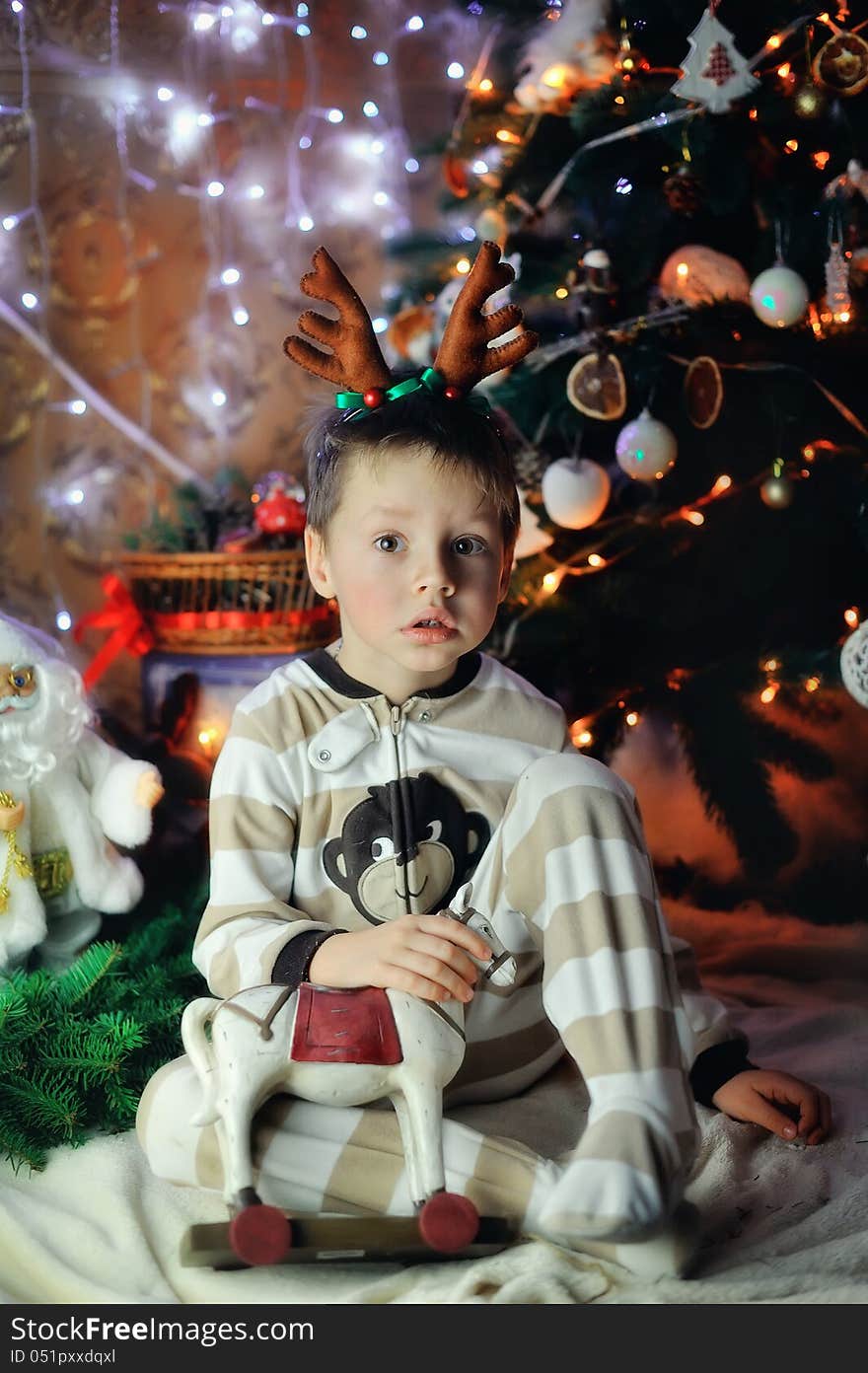 The boy sits with beautiful toys under a fur-tree with small horns on a head. The boy sits with beautiful toys under a fur-tree with small horns on a head