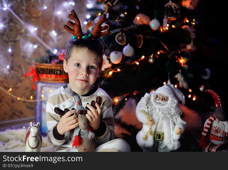 The boy sits with beautiful toys under a fur-tree with small horns on a head. The boy sits with beautiful toys under a fur-tree with small horns on a head