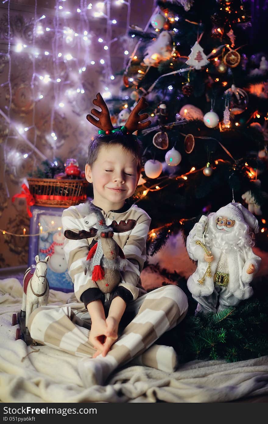 The boy sits with toys under a fur-tree with small horns on a head and dreams. The boy sits with toys under a fur-tree with small horns on a head and dreams