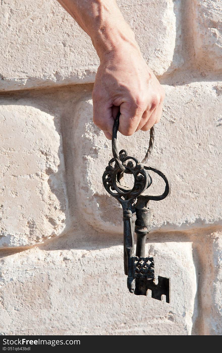 Hand holding vintage keys against a wall lined with white stones of the great. Hand holding vintage keys against a wall lined with white stones of the great