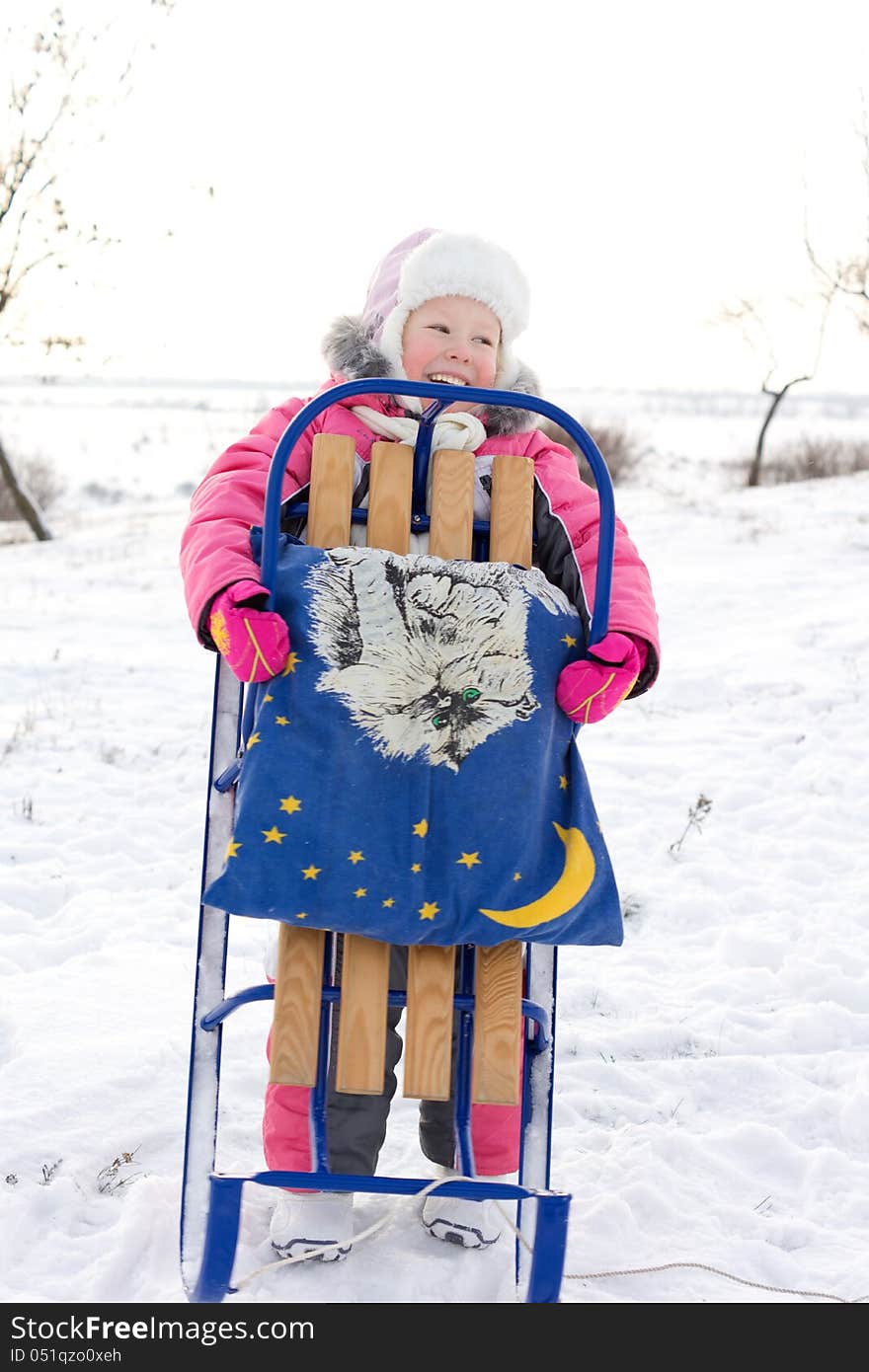 Merry little girl holding her winter sled up in front of her laughing and looking out of the frame