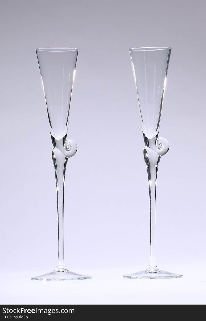 TWo Champagne glasses, lit partly from behind, empty in front of neutral, light grey background. TWo Champagne glasses, lit partly from behind, empty in front of neutral, light grey background