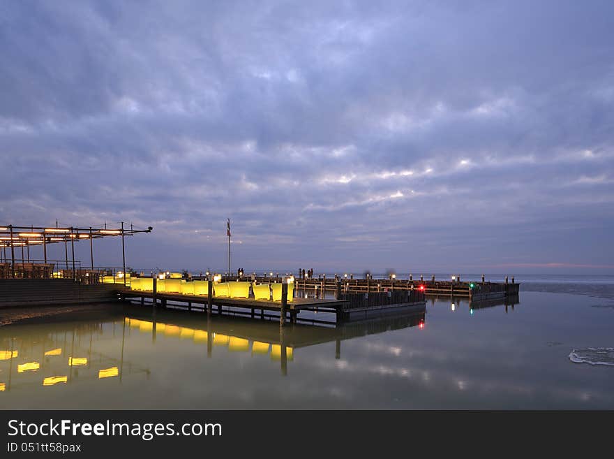 Beach Restaurant on the shore of a big lake on winter evening. The outside-seats are made of translucent plastic and lit from the inside, the light is reflected on the water. Beach Restaurant on the shore of a big lake on winter evening. The outside-seats are made of translucent plastic and lit from the inside, the light is reflected on the water.