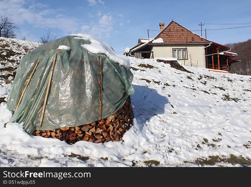 Pile of wood for winter covered with plastic near house