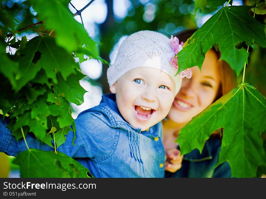 Little laughing girl looking through leaves of a tree, she is happy. Little laughing girl looking through leaves of a tree, she is happy