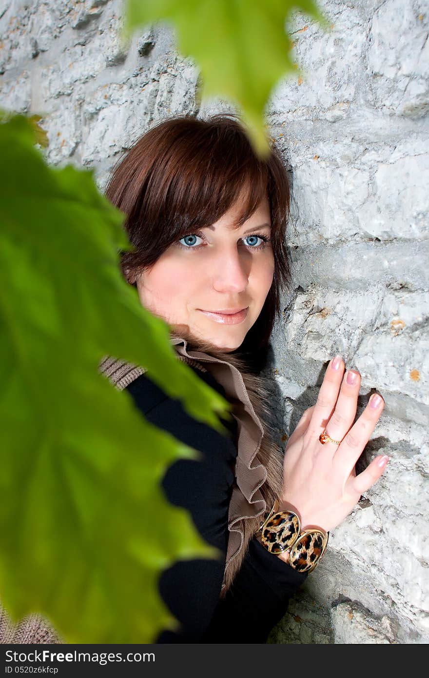 Beautiful blue-eyed smiling girl outdoors near the wall and maple. Beautiful blue-eyed smiling girl outdoors near the wall and maple